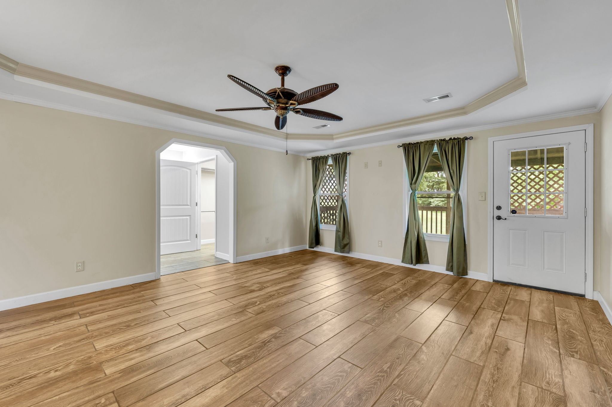 Empty room with wood-look flooring, a tray ceiling fan, green curtains, and a glass-panel door.