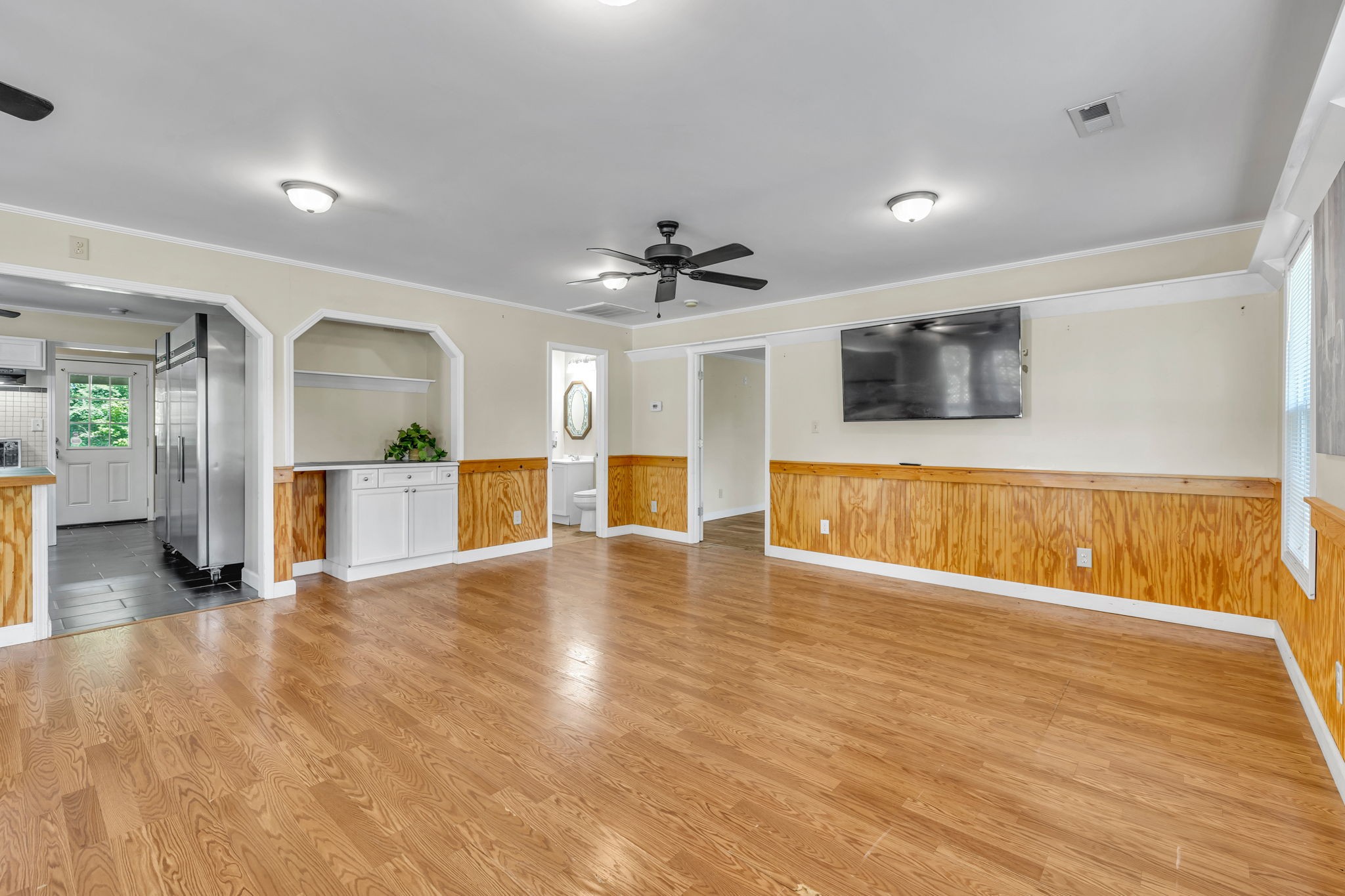 Living room with hardwood floors, wood wainscoting, ceiling fan, and wall-mounted television.