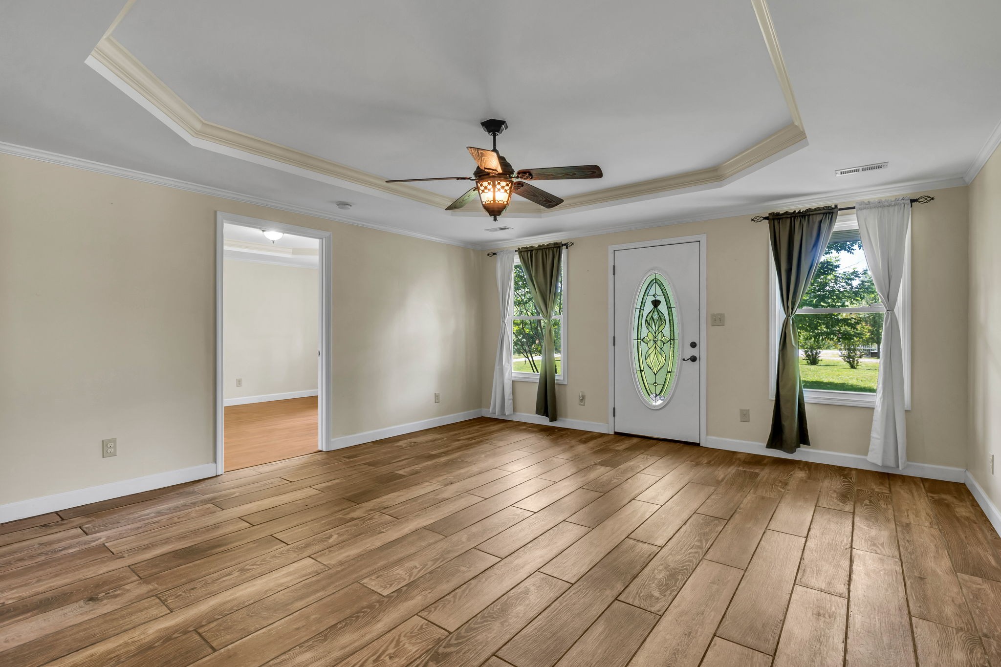 Empty living room with wood-look flooring, a tray ceiling, and a decorative glass front door.
