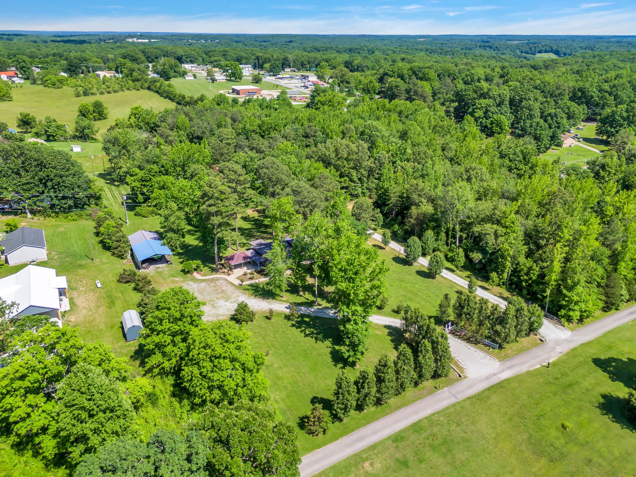 Aerial view of a rural property with wooded acreage, open lawns, and several outbuildings.