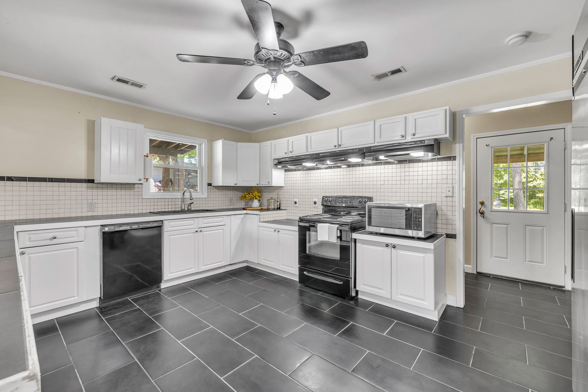 Kitchen with white cabinets, dark tile flooring, black range, and a glass-paneled exterior door.