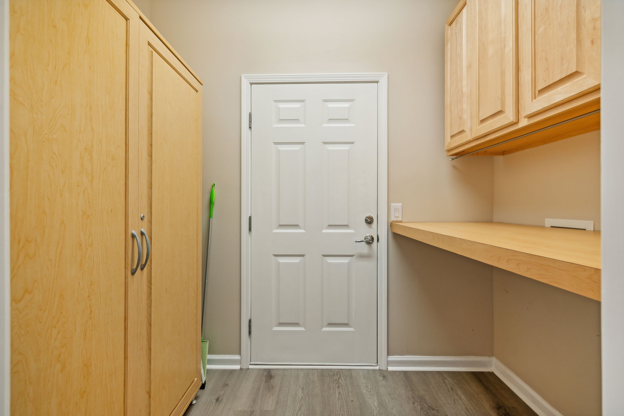 Entry mudroom with light-wood cabinets and counter beside a white paneled door.