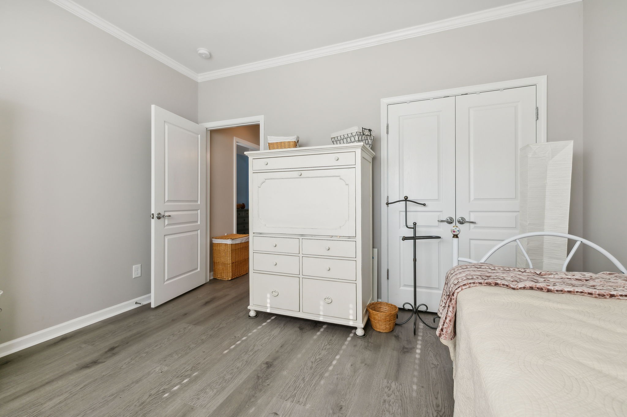 Bedroom with white bed and dresser, gray wood-look flooring, and double closet doors.