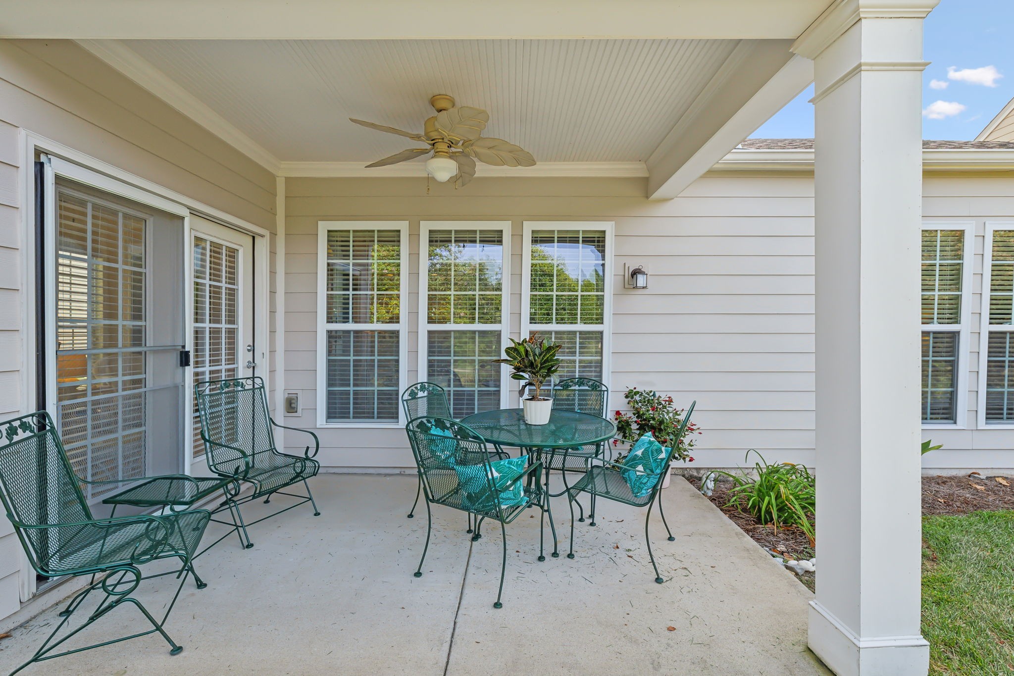 Covered patio with green metal dining set, ceiling fan, and potted plants.