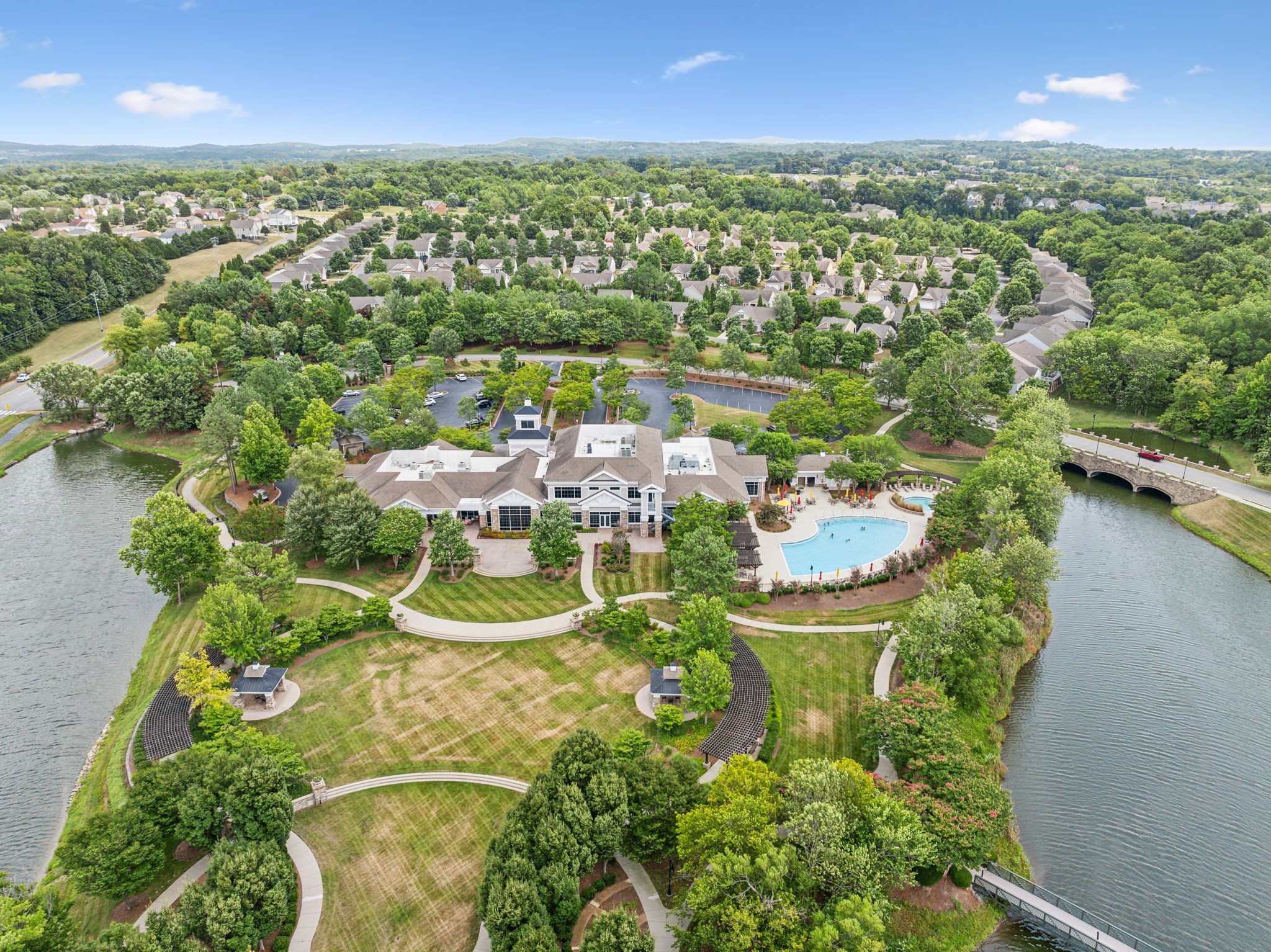 Aerial view of a lakeside community clubhouse with a swimming pool, landscaped grounds, and surrounding homes.