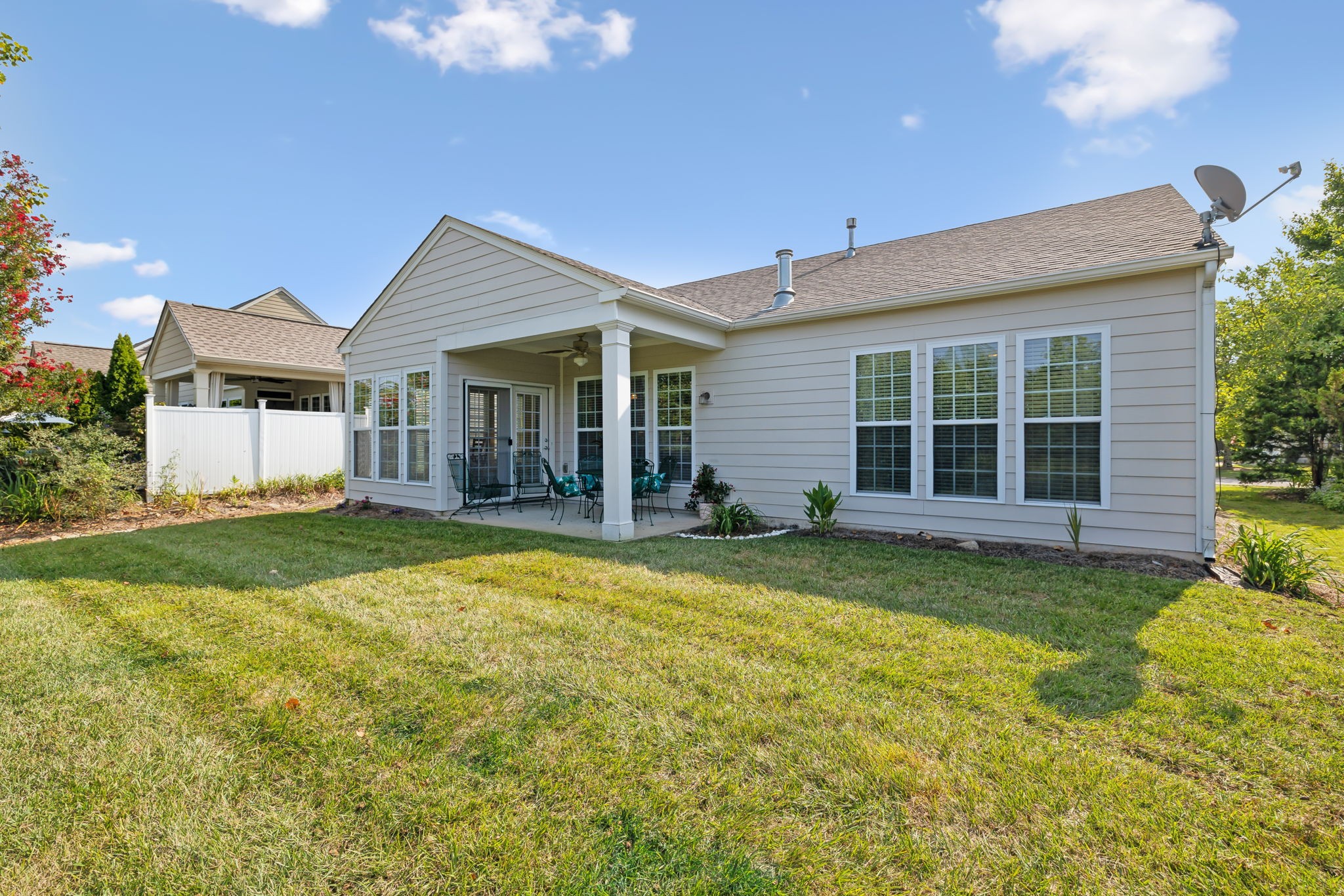 Rear of a light-gray home with a covered patio, outdoor seating, and a broad lawn.