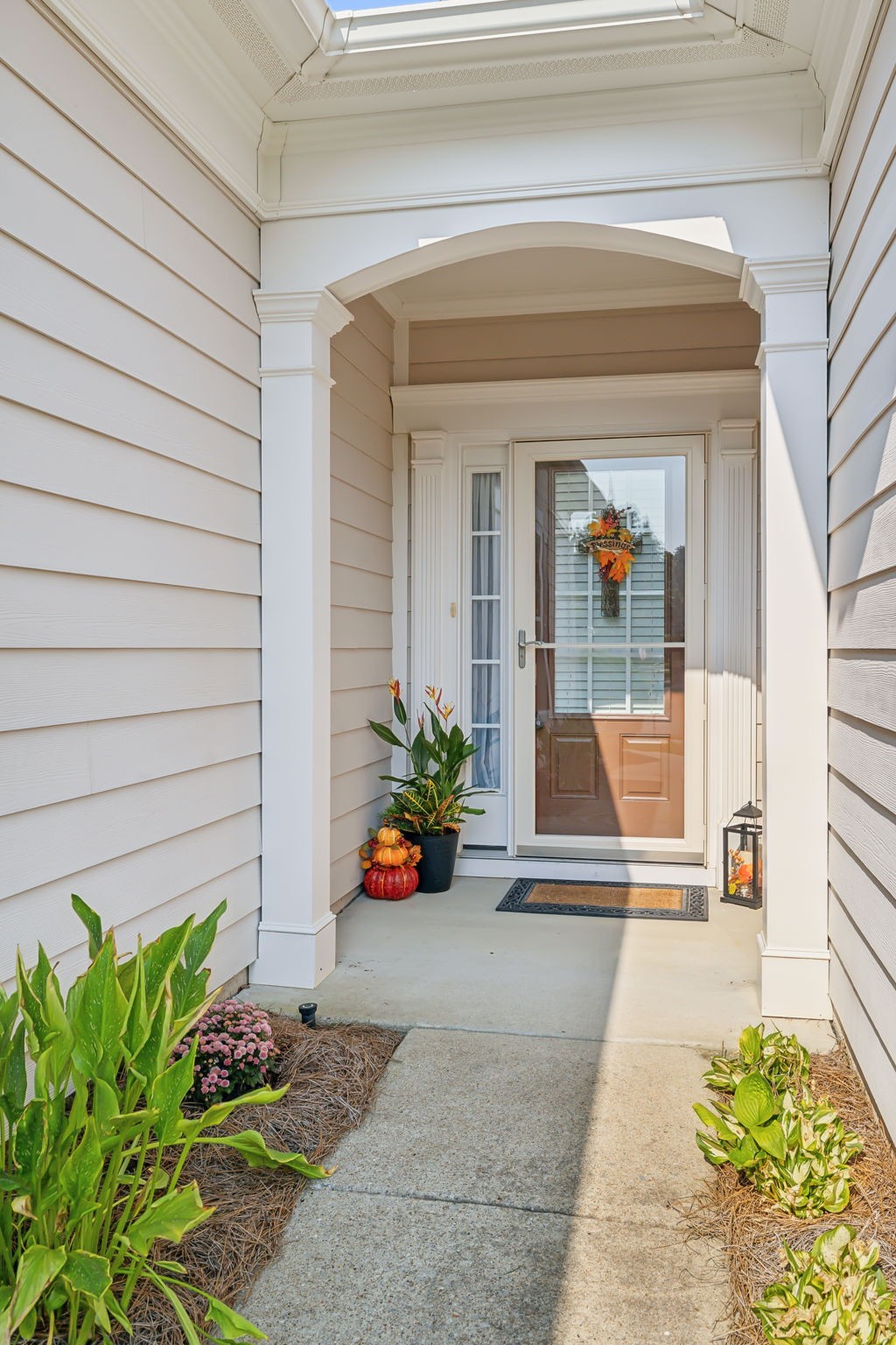 Covered front entry with an arched porch, glass storm door, and autumn plants and pumpkins.