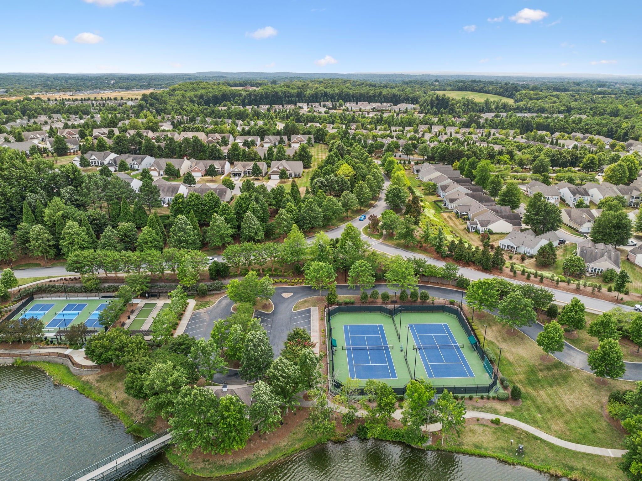 Aerial view of a leafy neighborhood with tennis courts beside a lake.