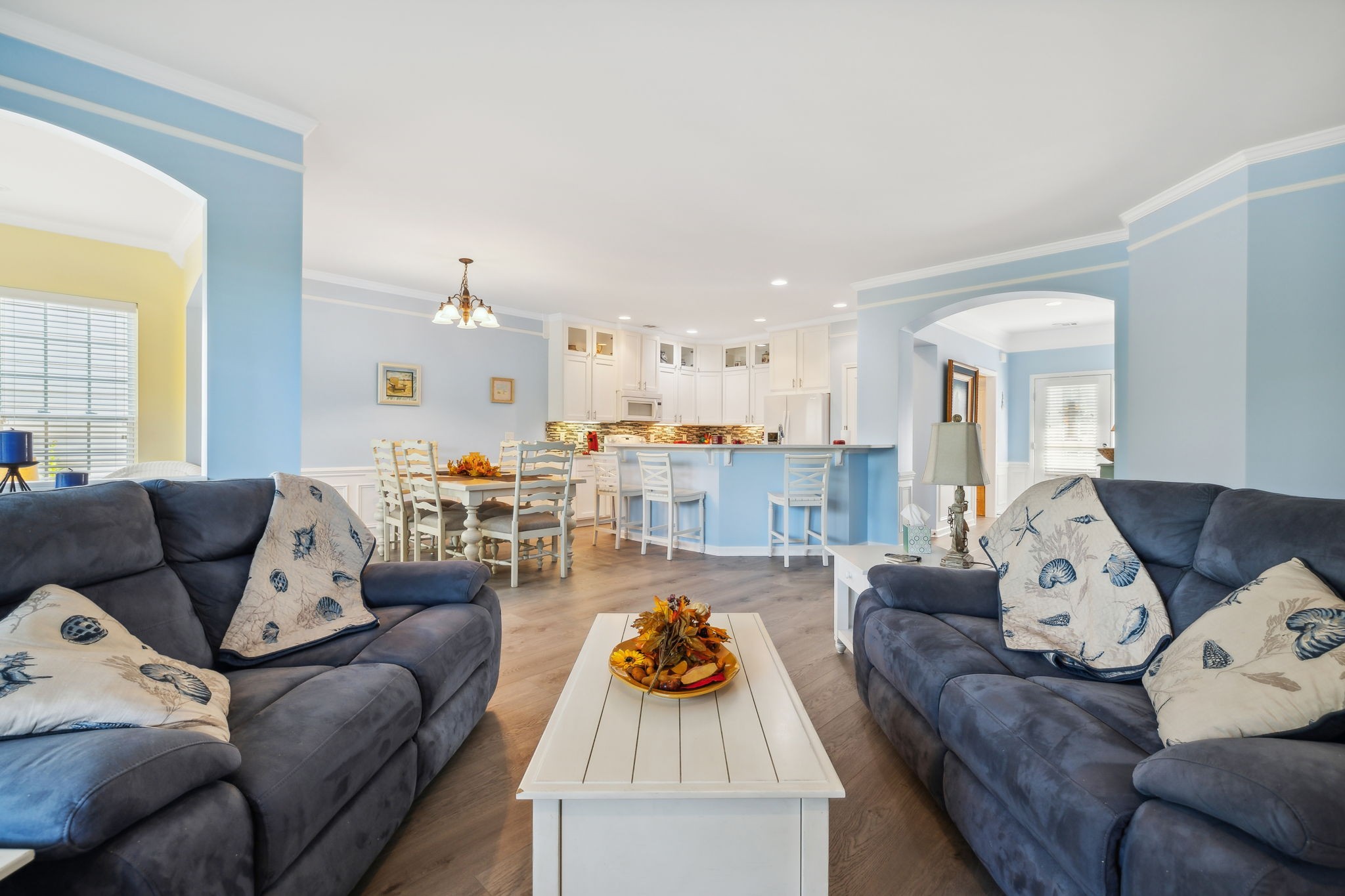 Open-plan living room with dark sofas, a white coffee table, and a kitchen breakfast bar.