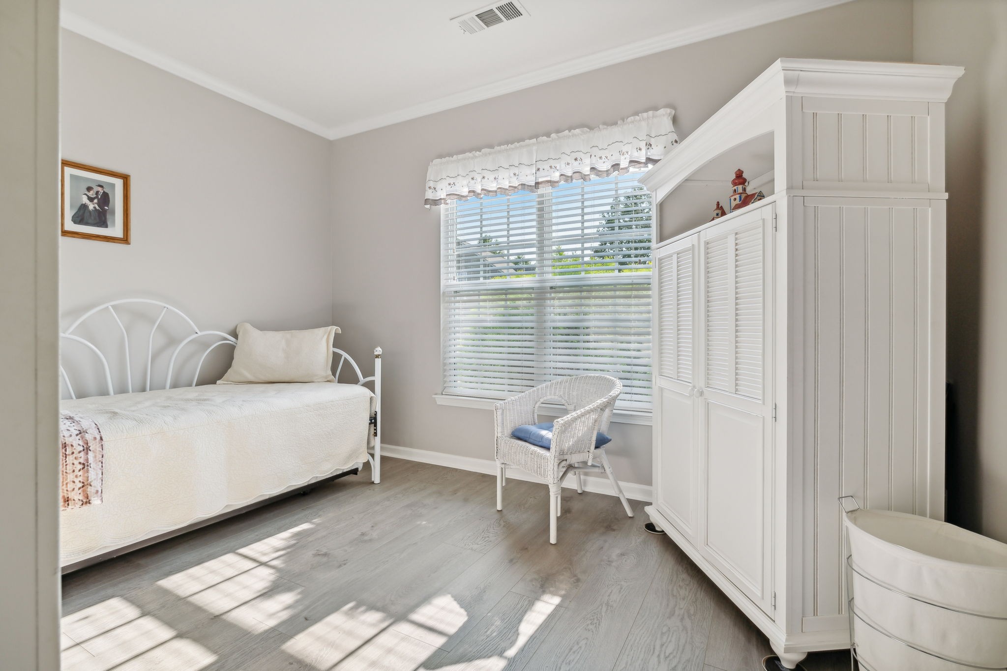 Bright bedroom with a white daybed, wicker chair, and large built-in wardrobe.