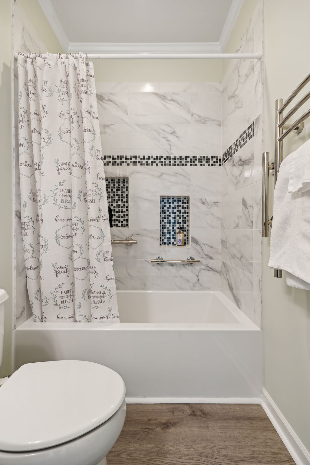 Bathroom with a white tub and marble-look shower tile, mosaic accents, and recessed niches.