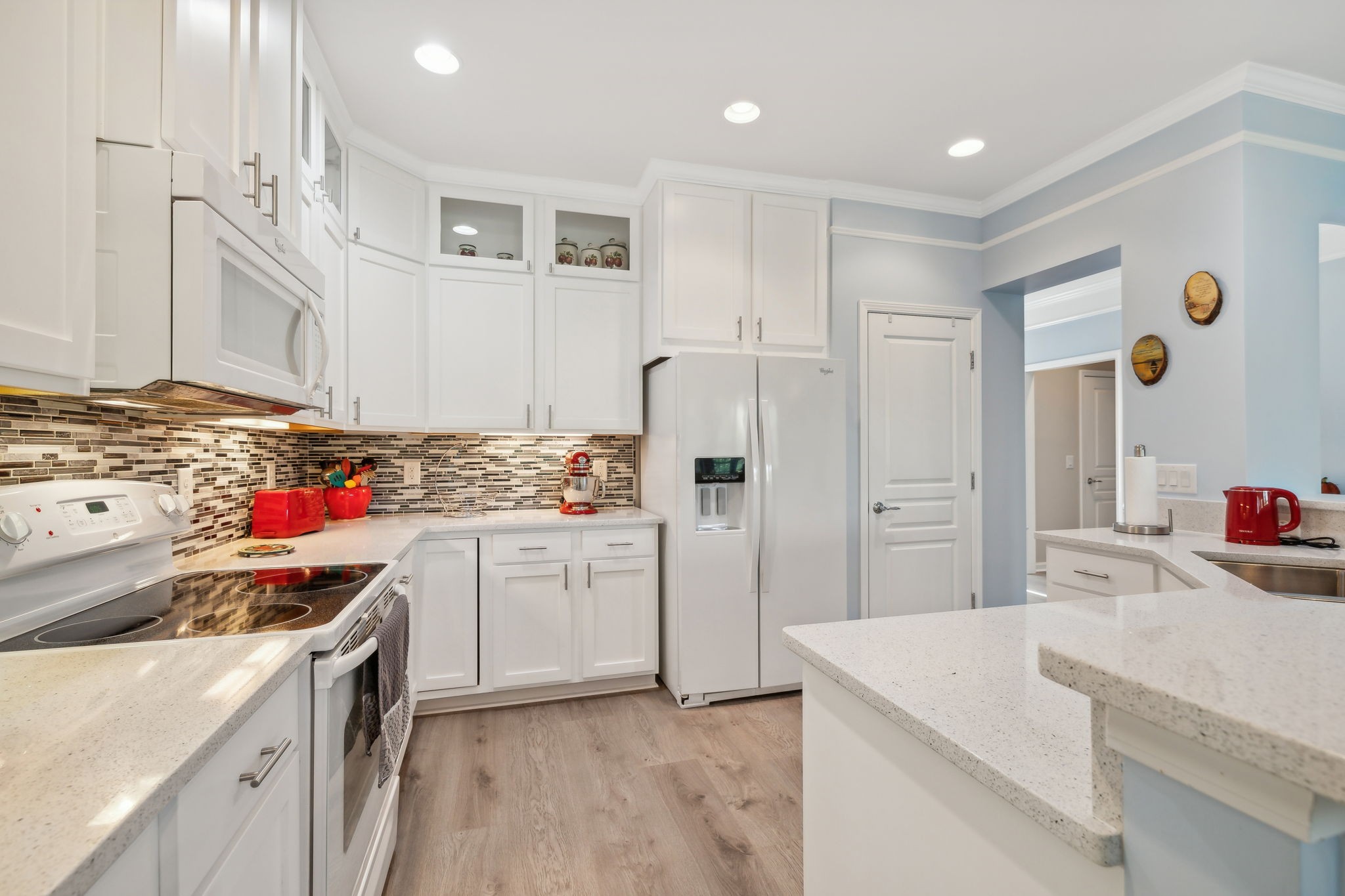 Bright white kitchen with mosaic tile backsplash, light countertops, and a large peninsula.