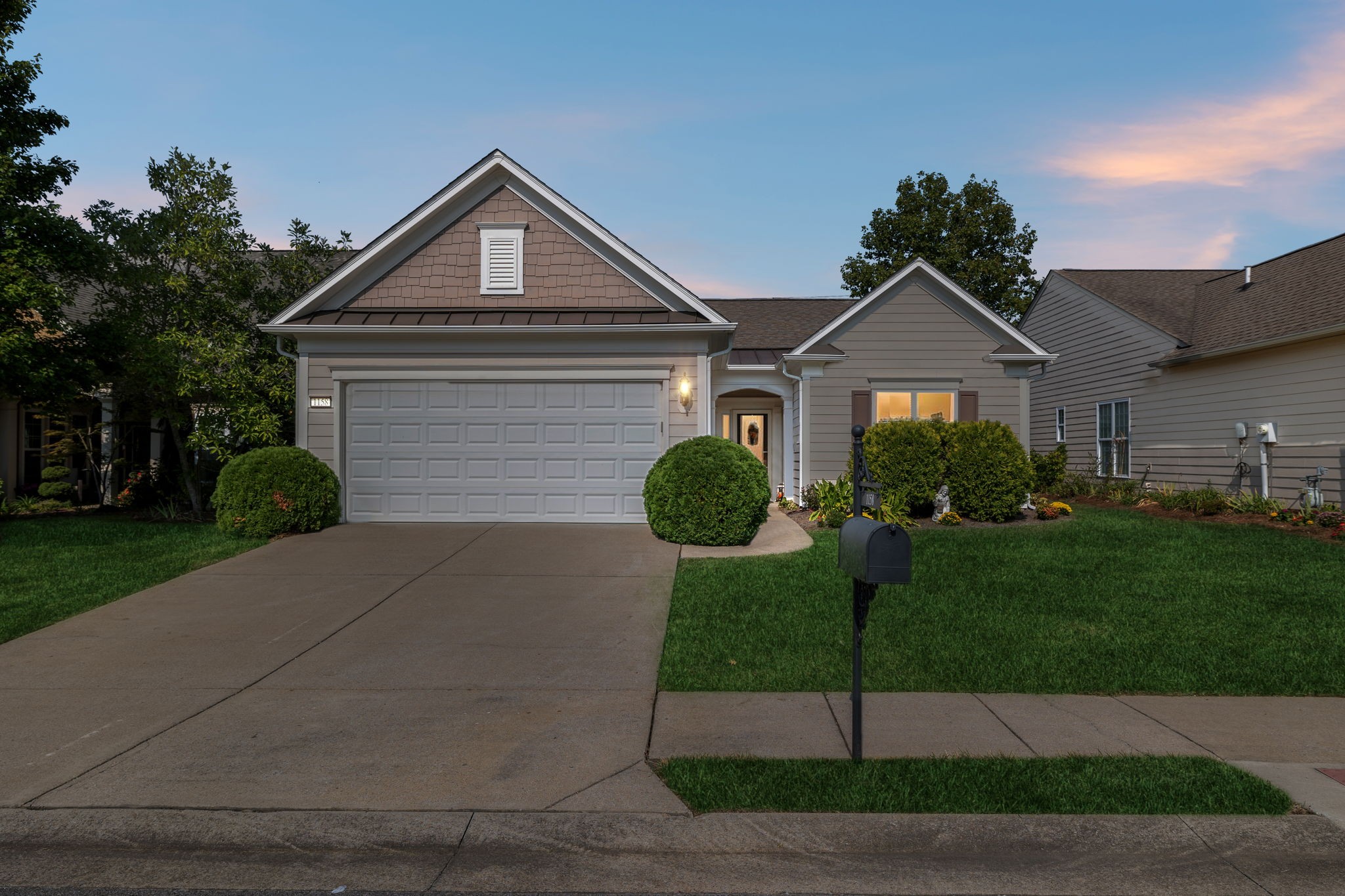 Gray single-story home with a two-car garage, landscaped front lawn, and mailbox at dusk.