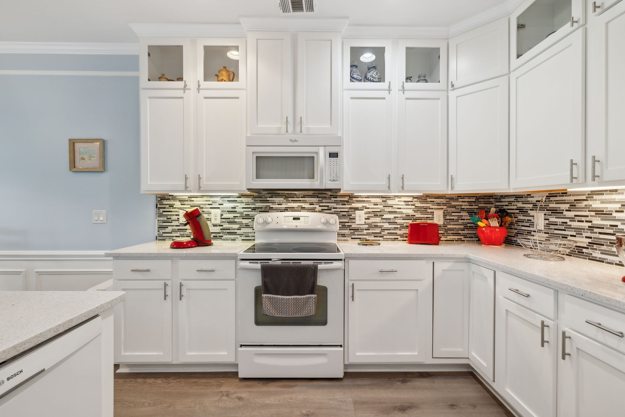 Kitchen with white cabinetry, mosaic tile backsplash, and a white range and built-in microwave.