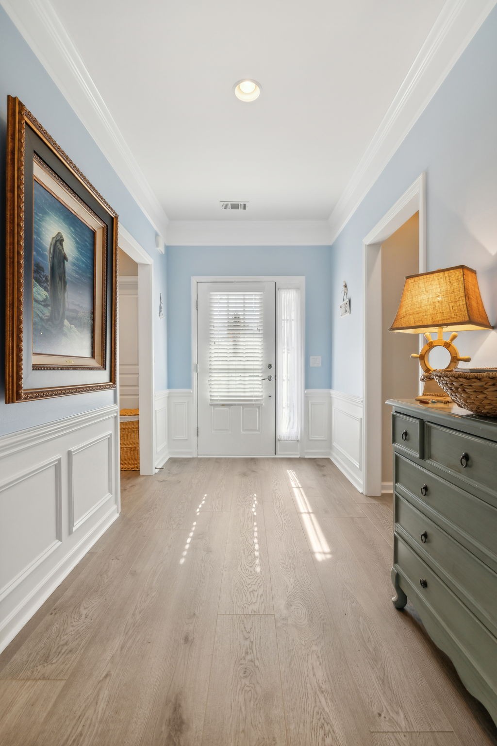 Entry foyer with pale blue walls, white wainscoting, and a white front door with blinds.
