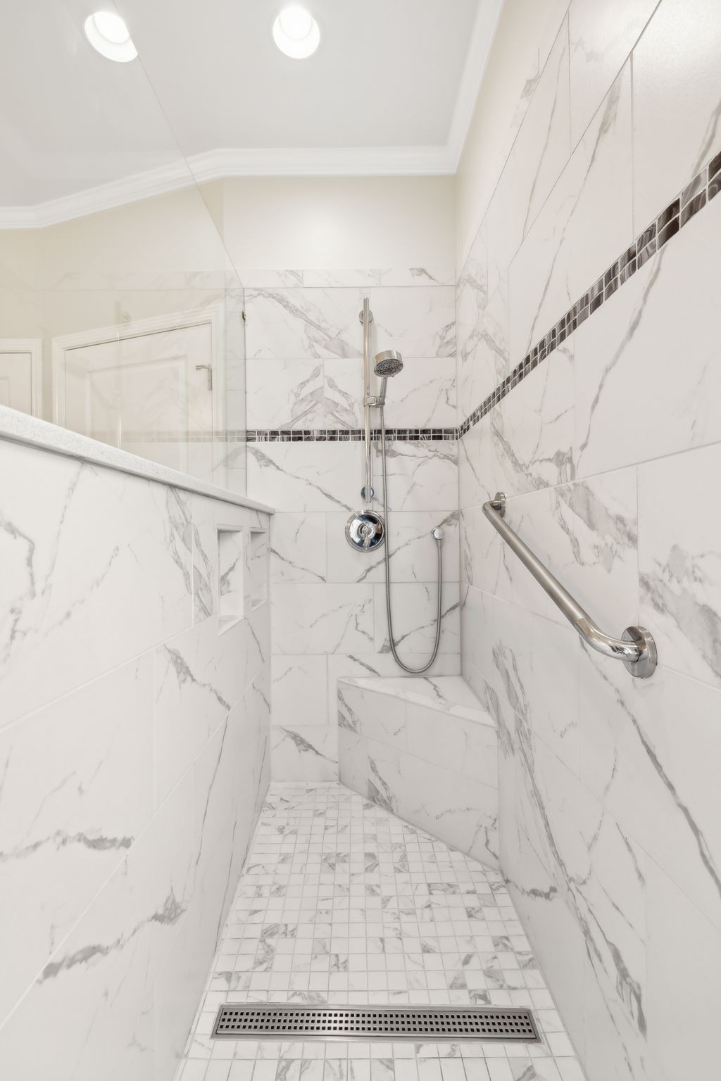 Walk-in shower with marble-look tile, a linear drain, built-in niches, and a metal grab bar.