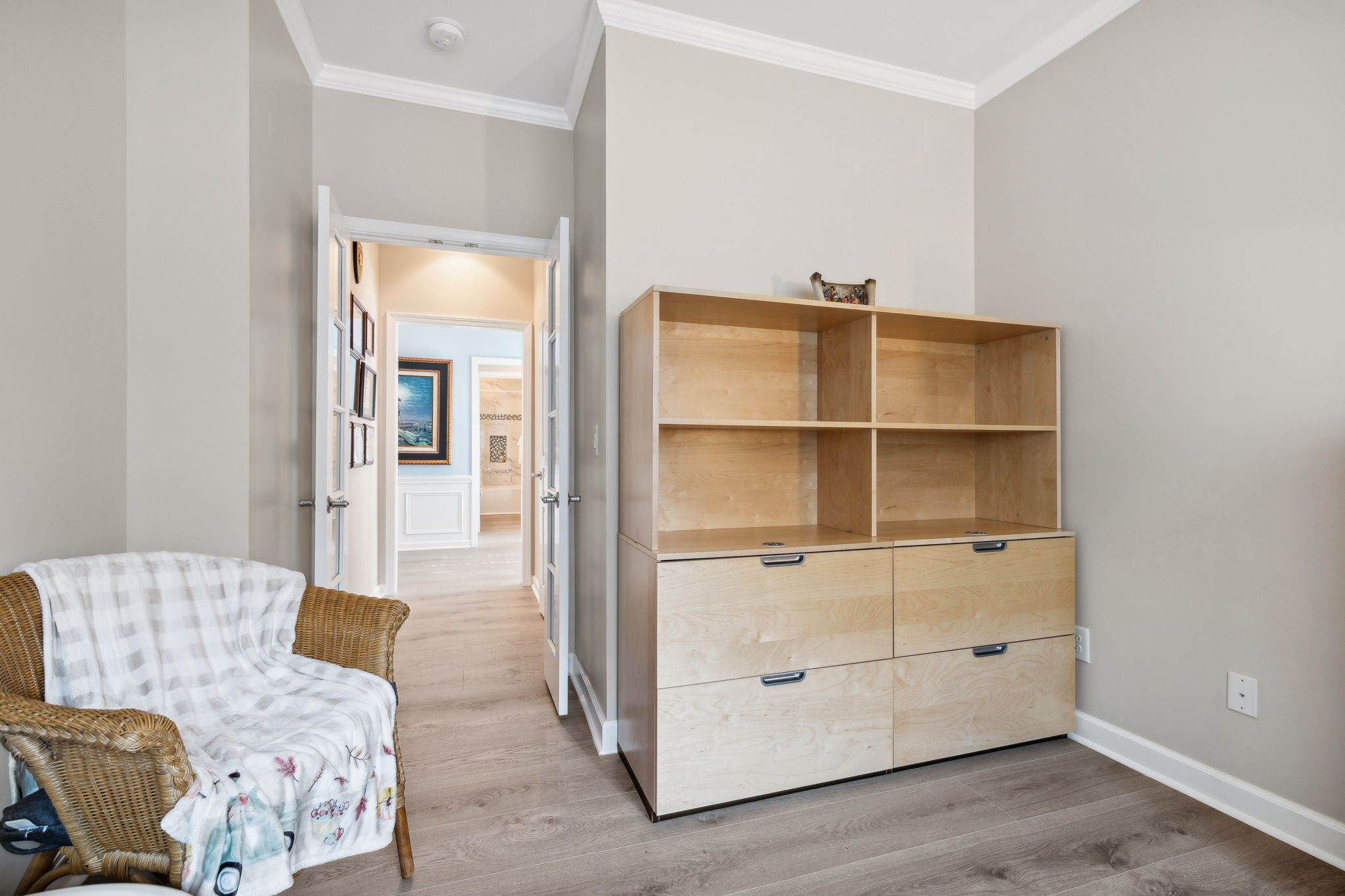 Furnished room with a light-wood cabinet and wicker chair beside open double doors.