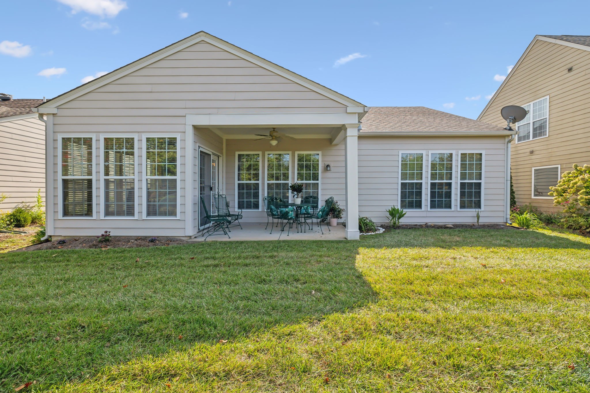 House rear with a covered, furnished patio and broad green lawn.