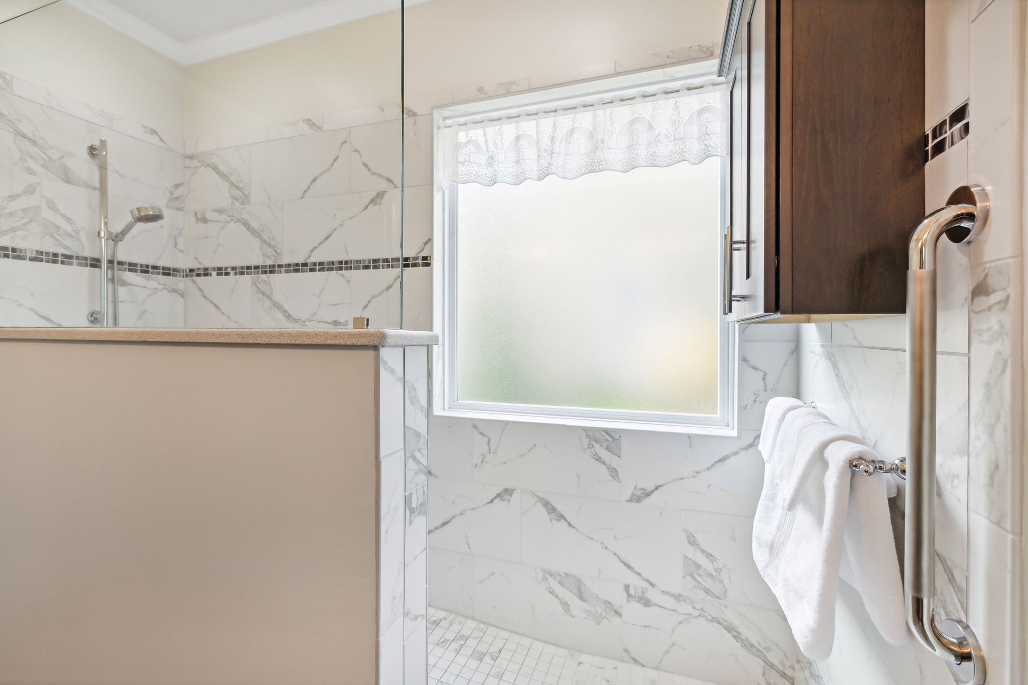 Bathroom shower with marble-look tile, frosted window, and chrome towel warmer.