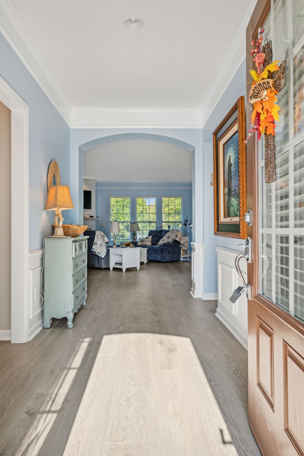 Entryway with an arched opening to a blue living room and sunlight across the floor.