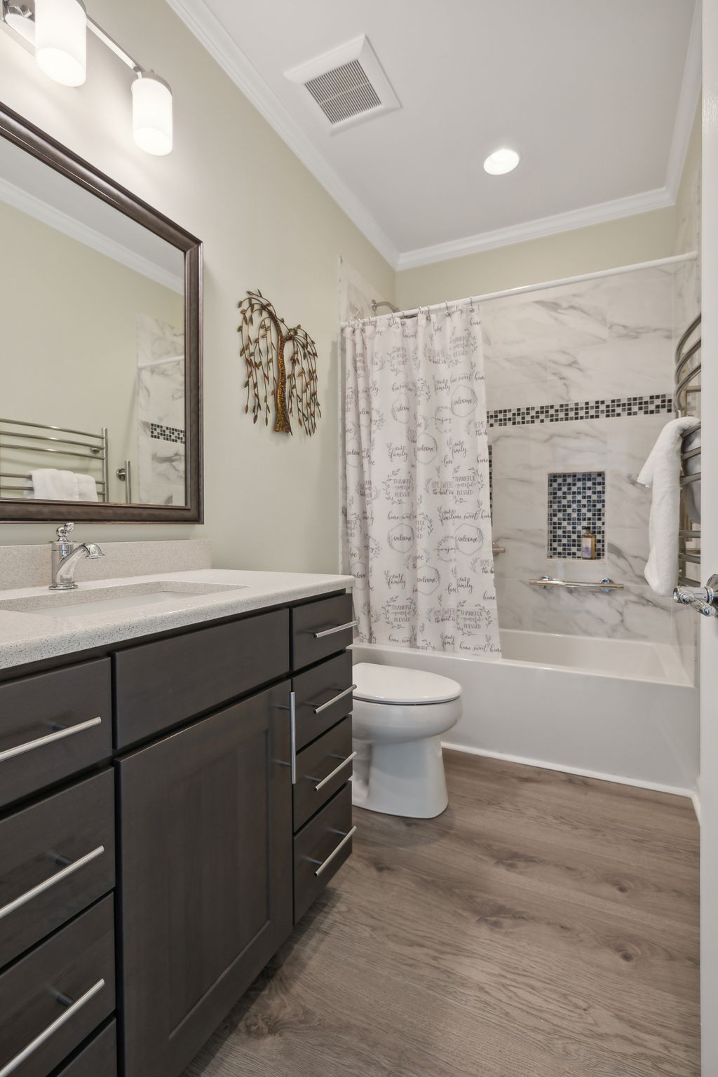 Bathroom with dark wood vanity, marble-look tub surround, mosaic niche, and wood-look flooring.