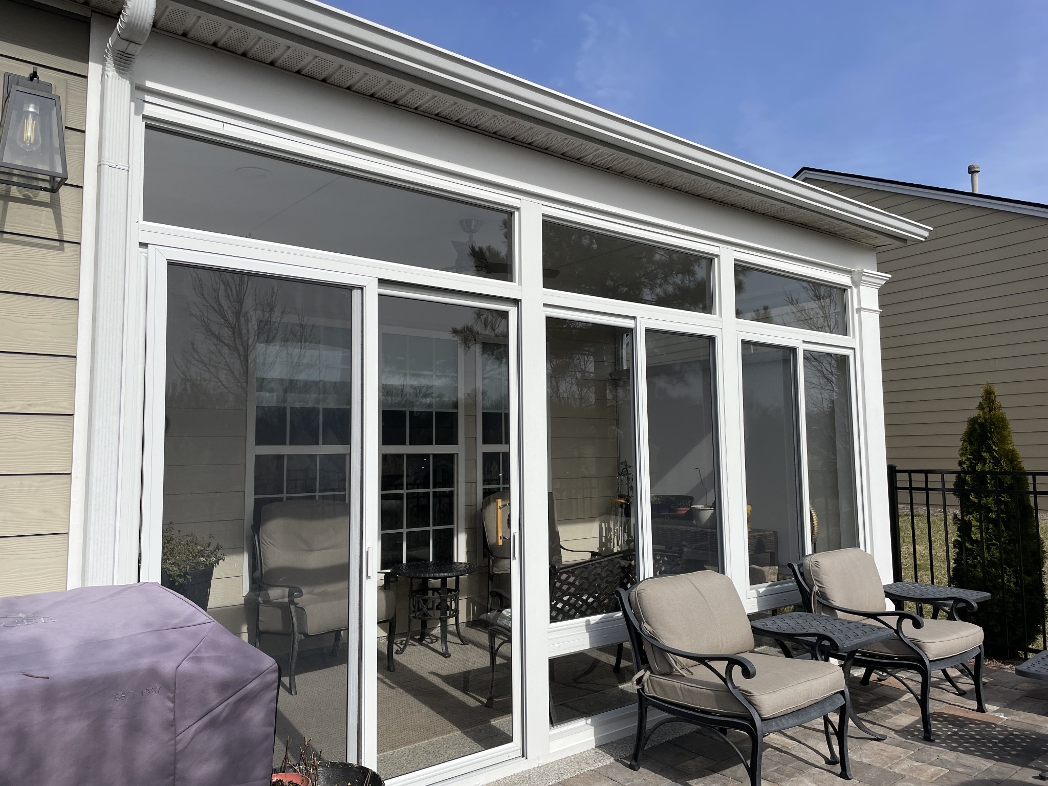 Stone patio with cushioned lounge chairs beside a sunroom with large windows and sliding glass doors.