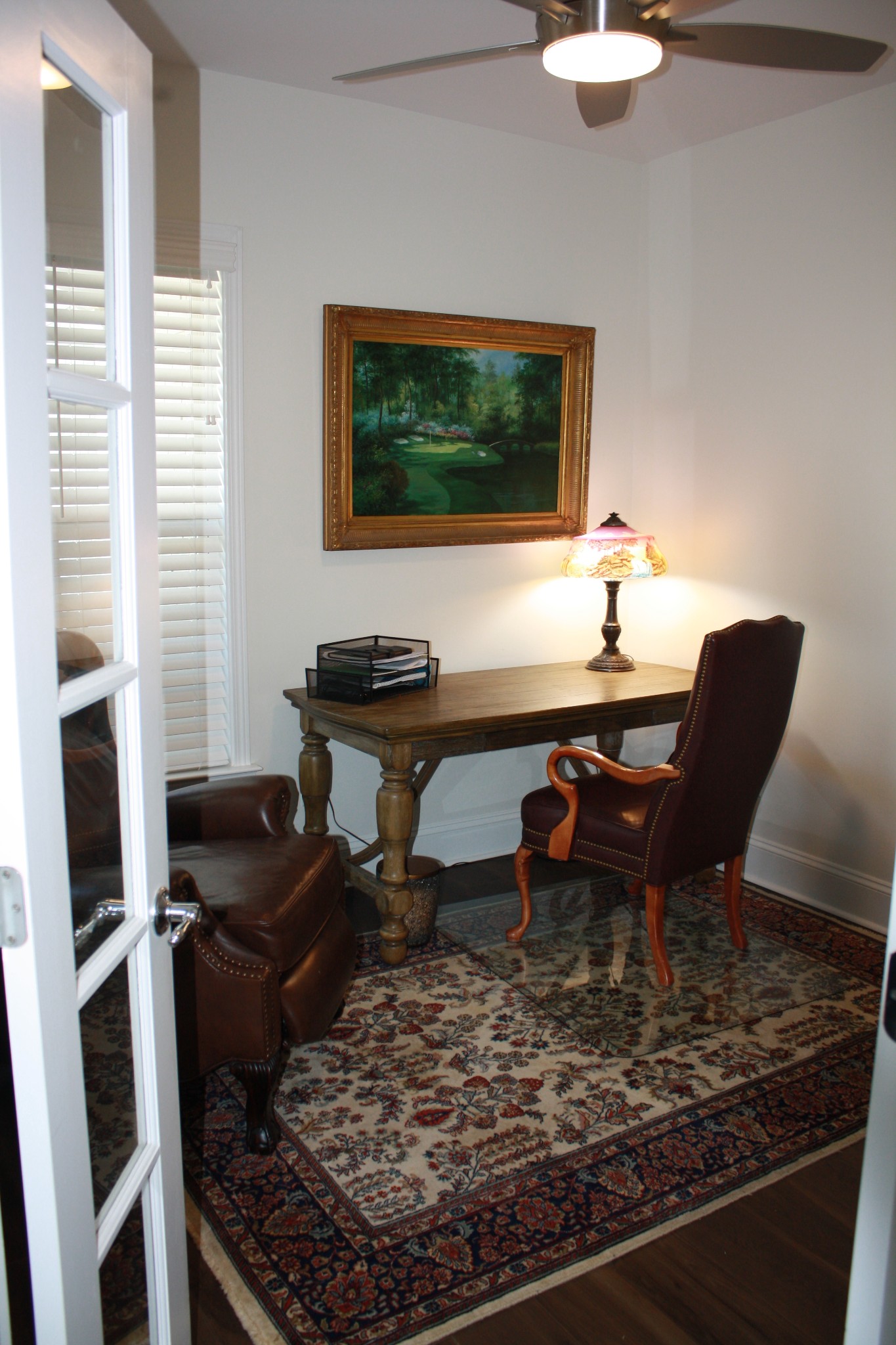 Furnished home office with a wooden desk, leather chair, and patterned rug.