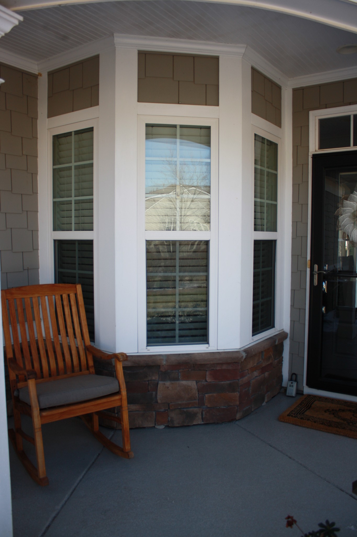 Covered porch with a stone-based bay window and wooden rocking chair beside the entry door.