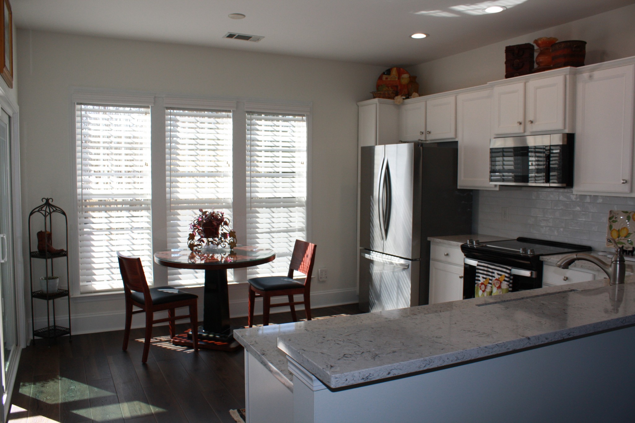 Kitchen with a large stone island, stainless steel appliances, and a dining nook by three windows.