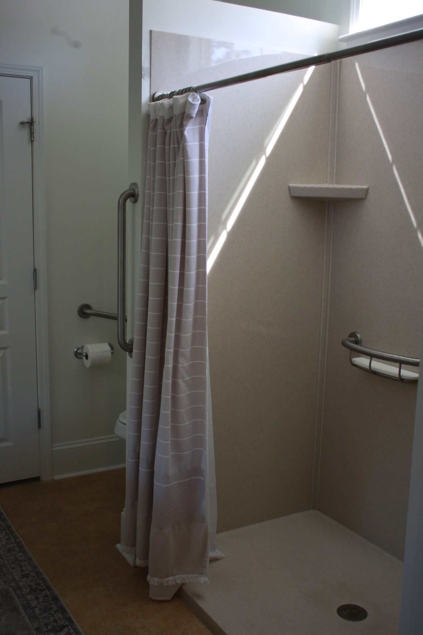 Walk-in shower with a striped curtain, built-in shelf, and metal grab bars.