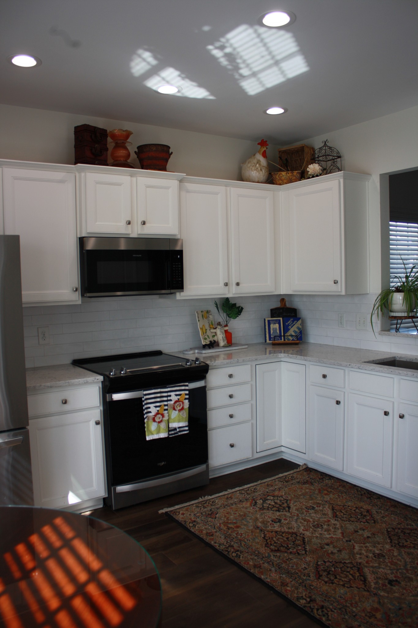 Kitchen with white cabinets, dark appliances, and a patterned rug on dark wood flooring.