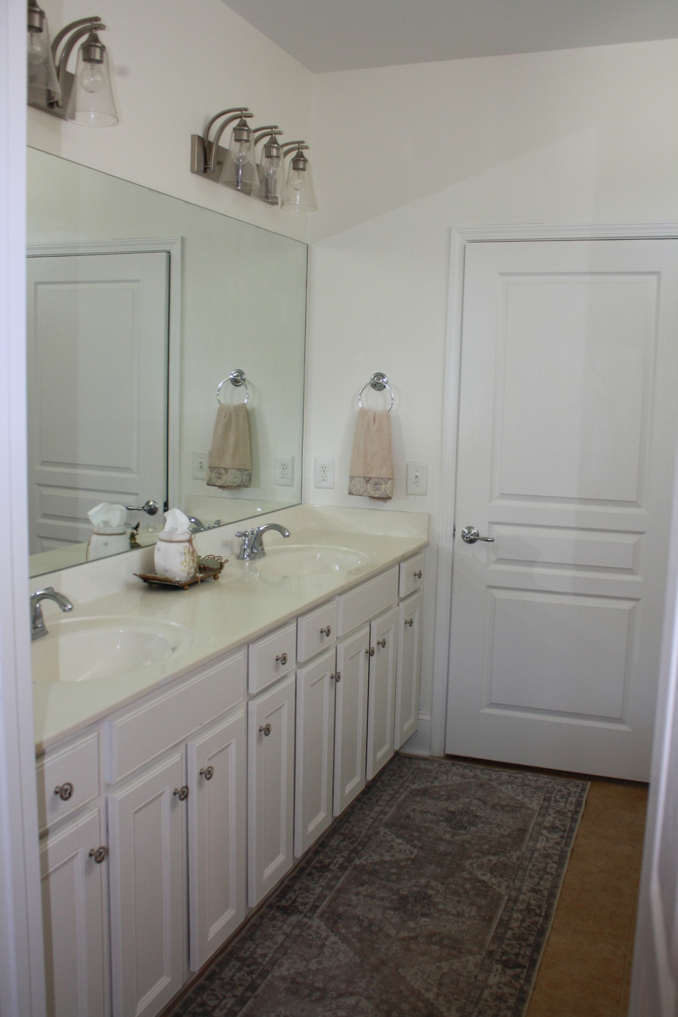 Bathroom with a white double-sink vanity, large mirror, chrome fixtures, and patterned runner rug.