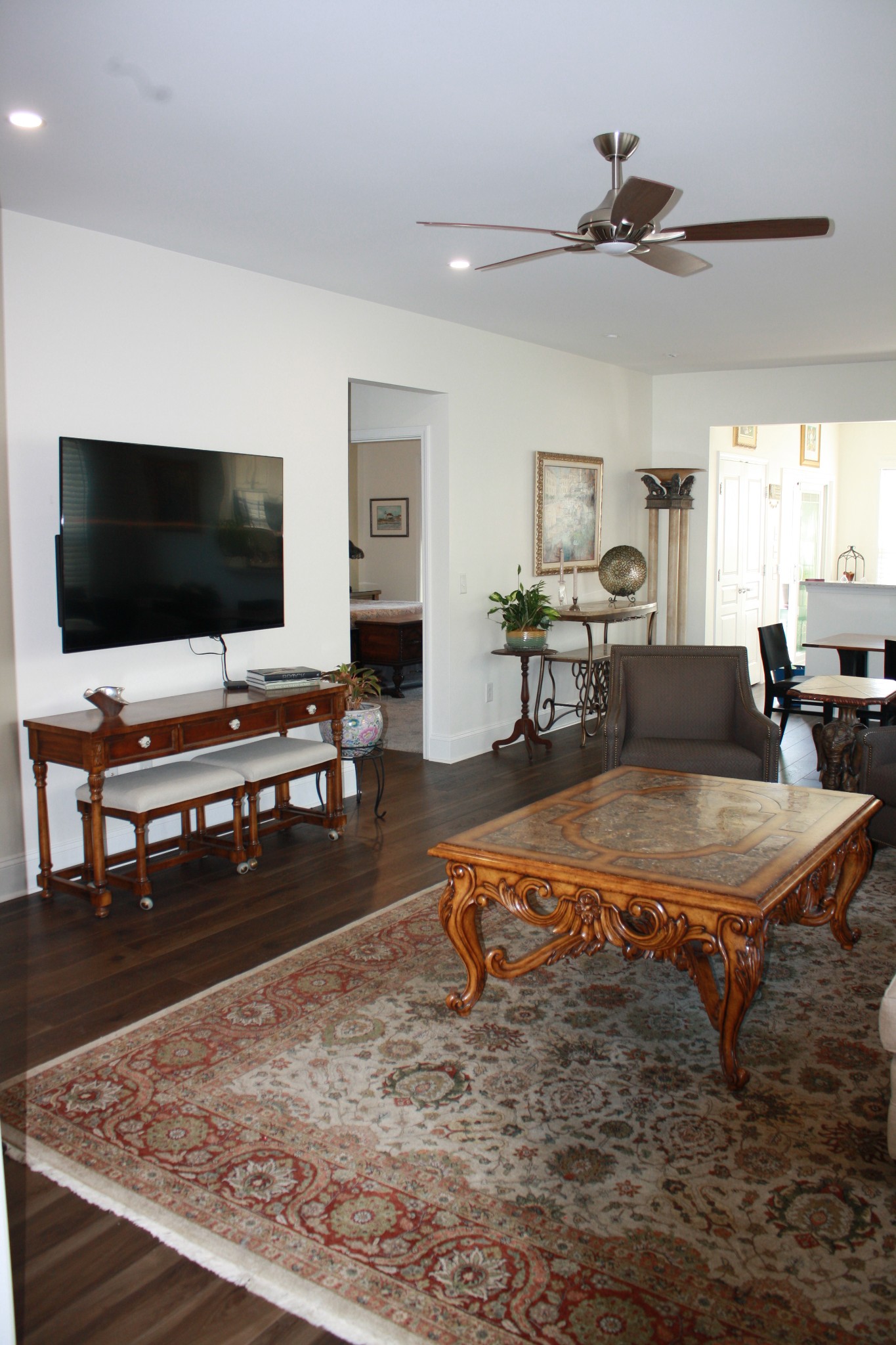 Furnished living room with an ornate coffee table, patterned rug, wall-mounted television, and ceiling fan.