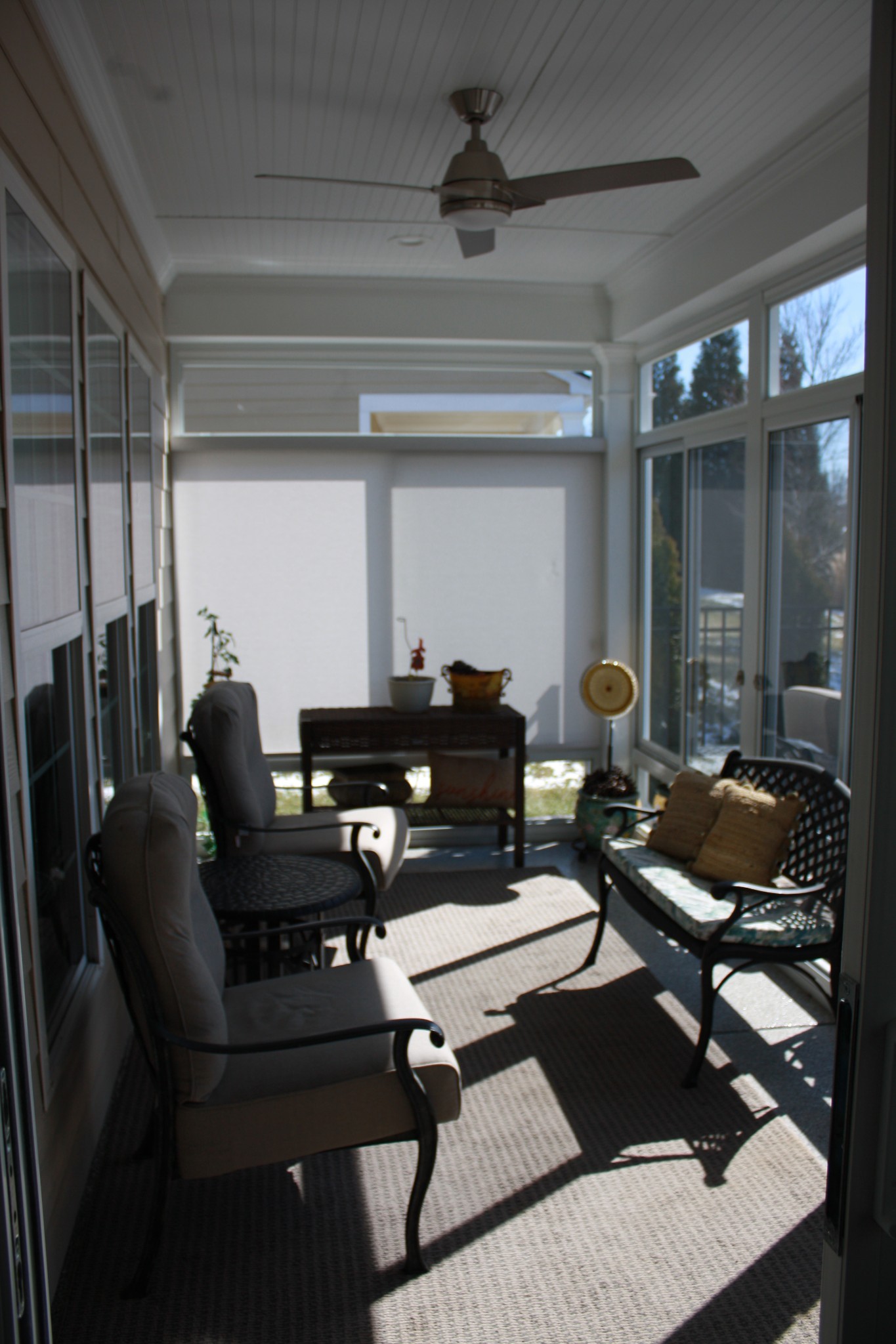 Furnished sunroom with large windows, a ceiling fan, cushioned seating, and sunlight across the rug.