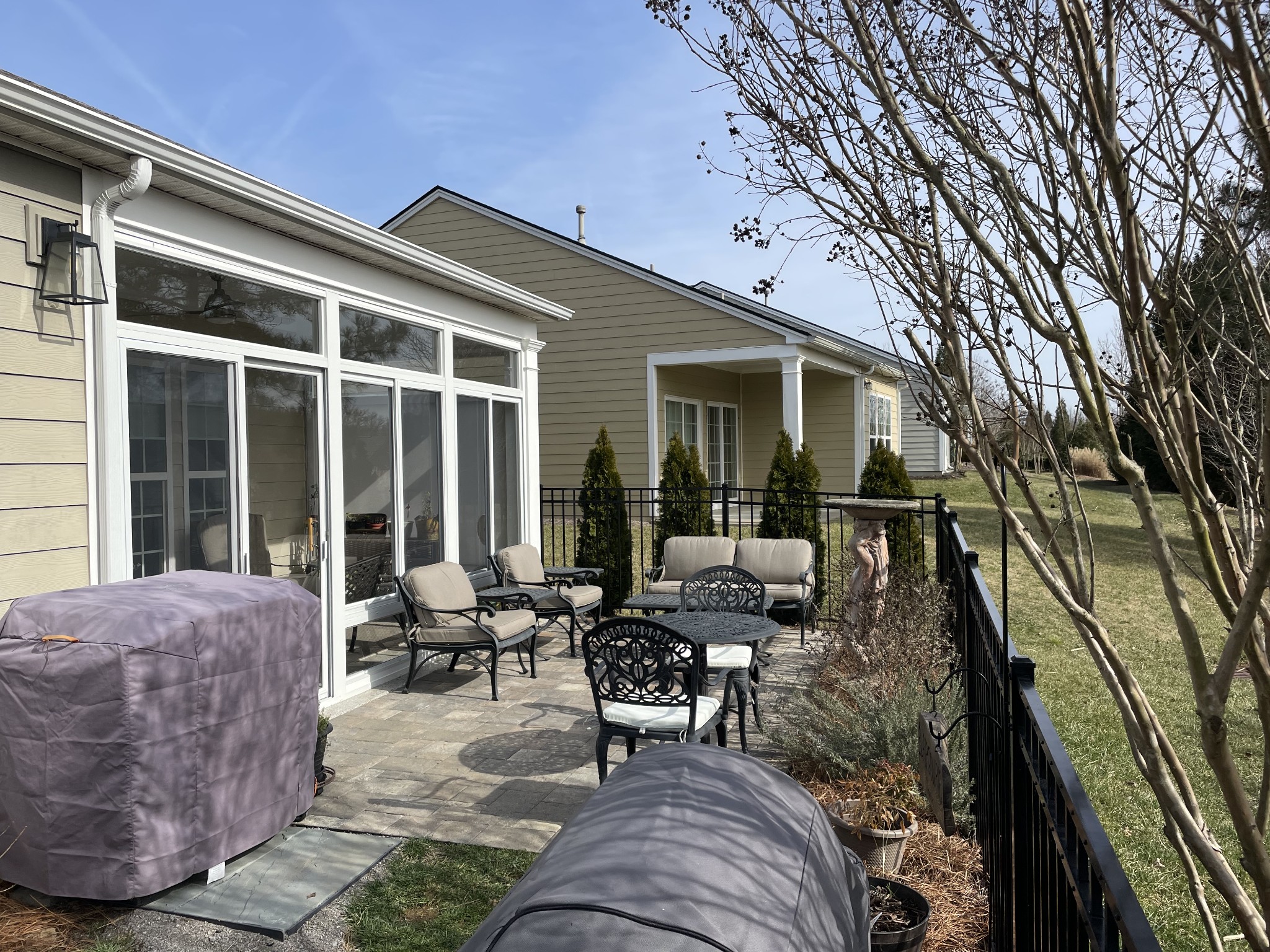 Stone patio with cushioned seating beside large windows, enclosed by a black metal railing.