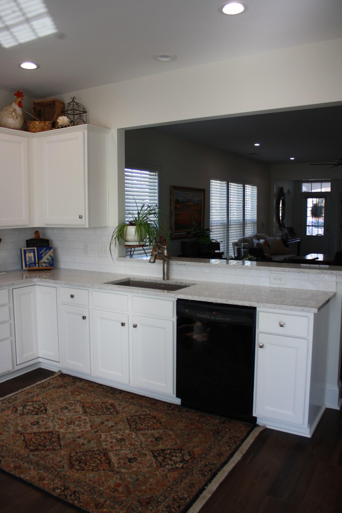 Kitchen with white cabinets, a stone countertop, black dishwasher, and a wide opening to the living room.