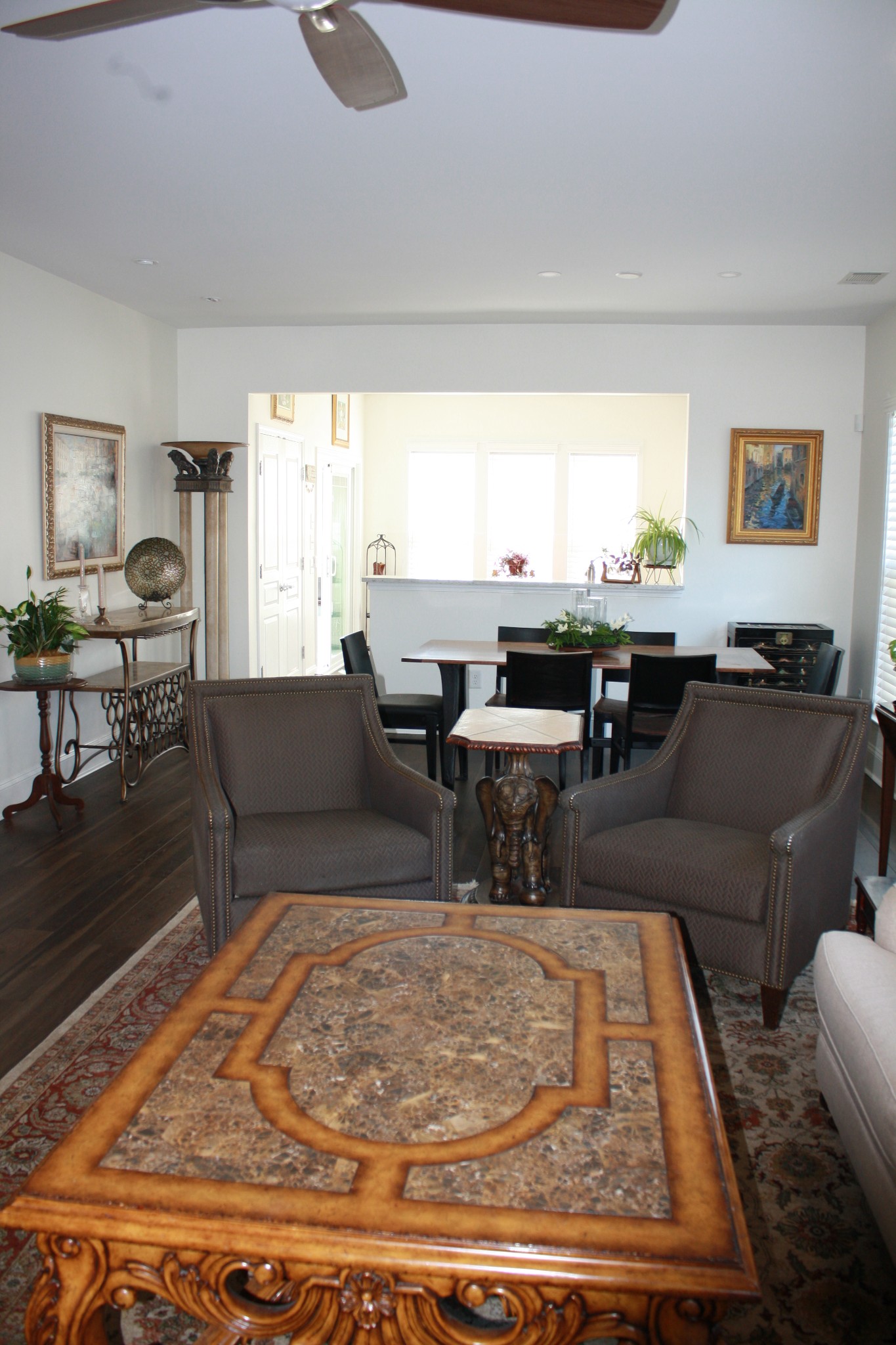 Furnished dining and sitting area with dark wood furniture, an ornate coffee table, and bright windows.