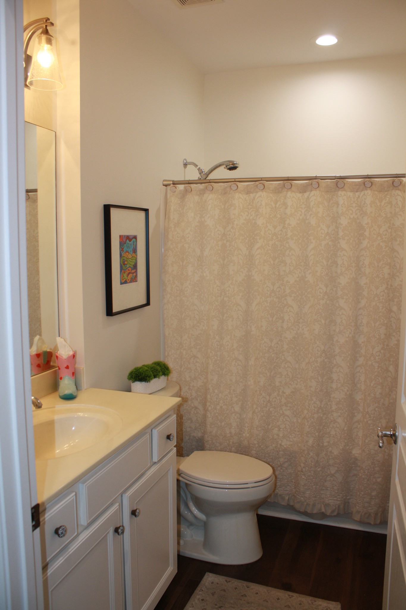 Bathroom with a white vanity, toilet, and patterned beige shower curtain.