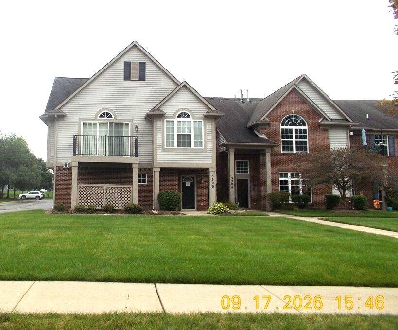 Two-story house with red brick, light siding, an upper balcony, and a broad green lawn.