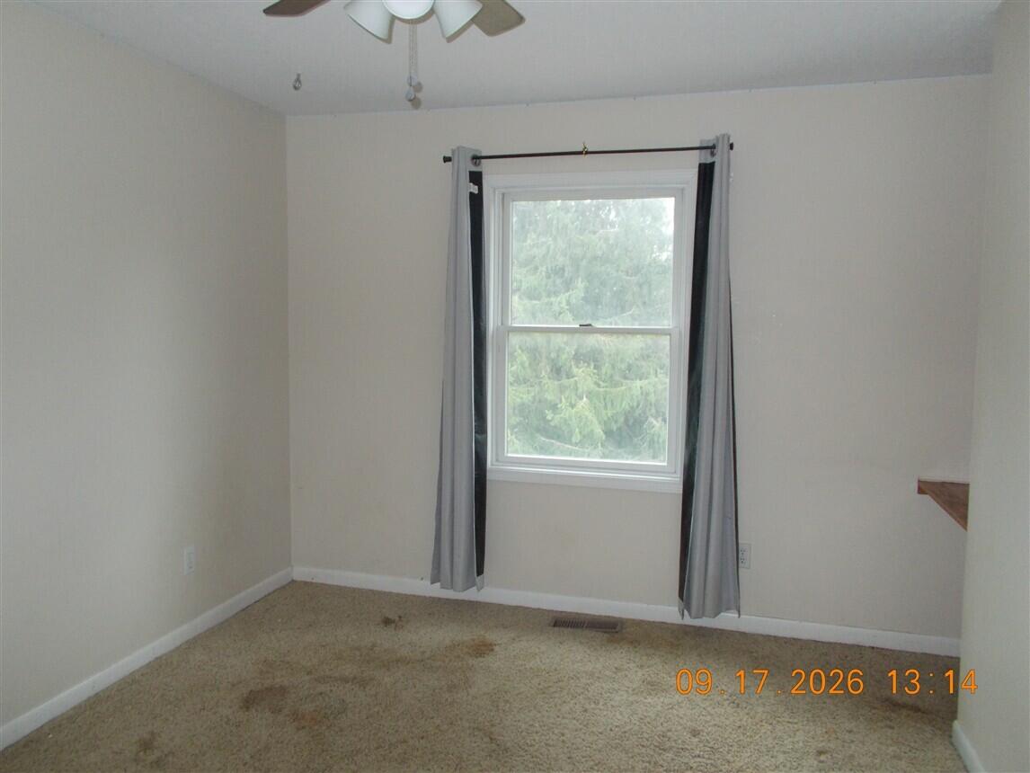 Empty bedroom with beige carpet and gray curtains framing a window overlooking trees.