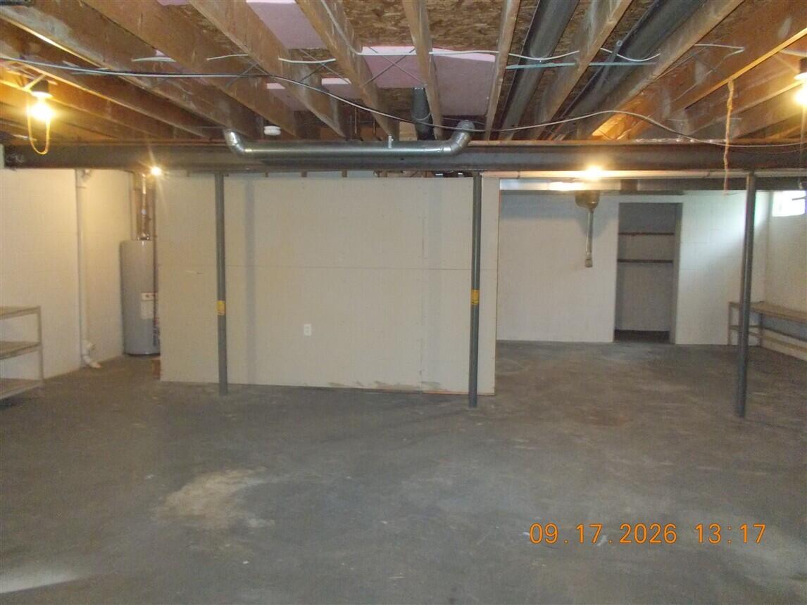 Unfinished basement with exposed ceiling joists, support posts, a concrete floor, and a water heater.