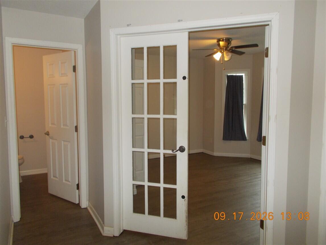Room with hardwood floors and a ceiling fan, viewed through white French doors.