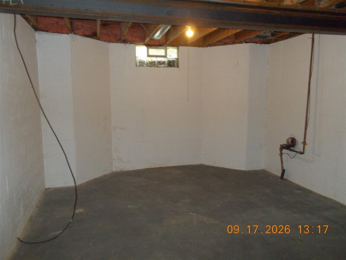 Unfinished basement with a concrete floor, exposed ceiling joists, and a small high window.