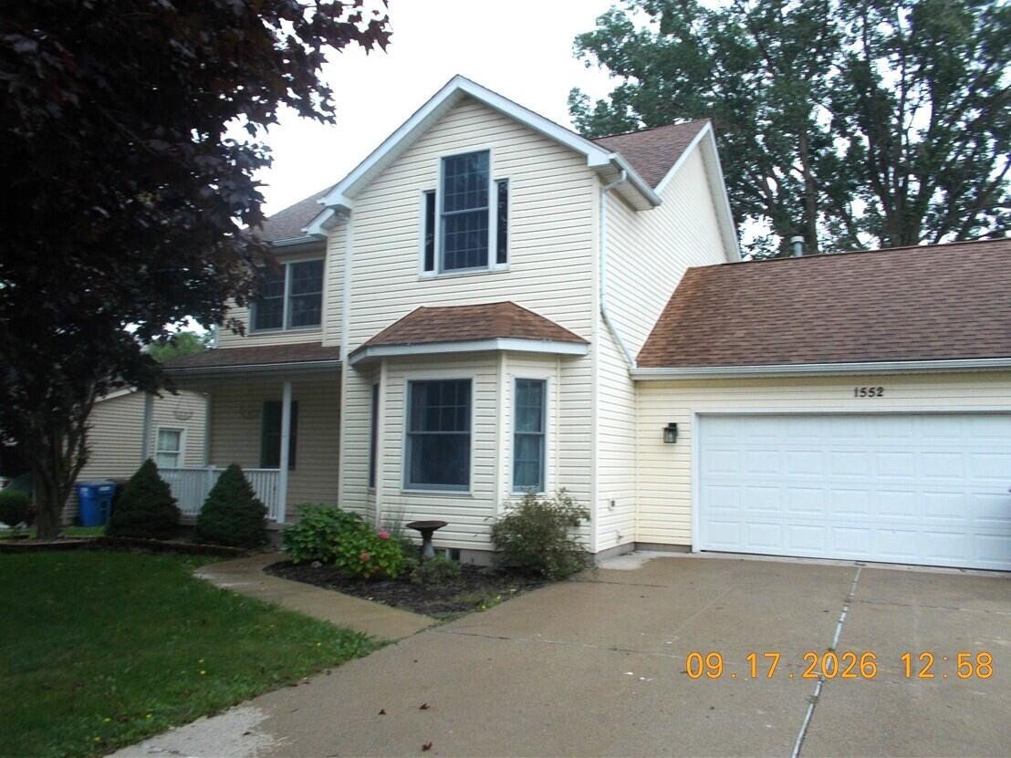 Cream two-story house with an attached garage, bay window, and landscaped front yard.