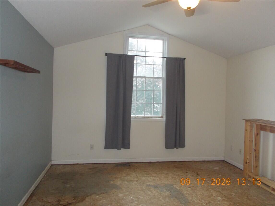 Empty room with vaulted ceiling, curtained window, ceiling fan, and unfinished flooring.