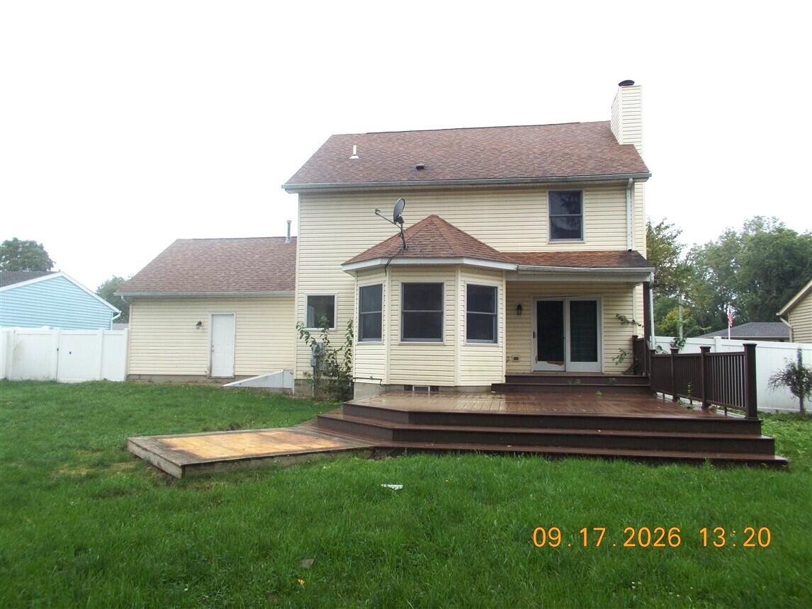 Rear of a beige two-story house with a bay window and broad wooden deck.