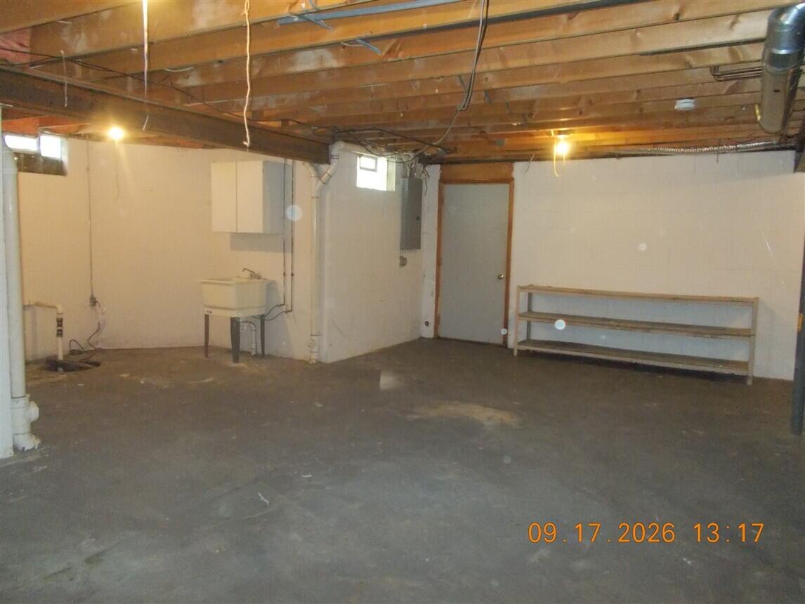 Unfinished basement with exposed ceiling joists, a concrete floor, and a utility sink.
