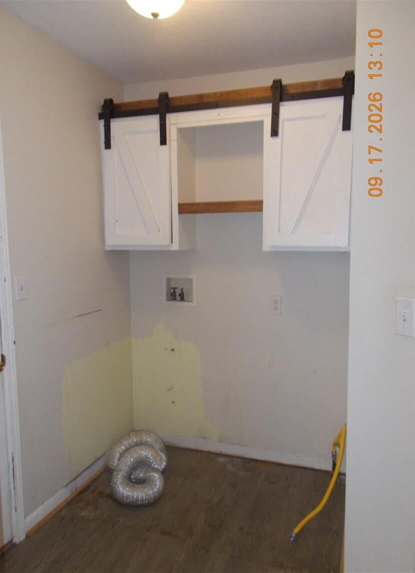 Utility nook with white barn-style cabinets, washer hookups, and unfinished walls and flooring.