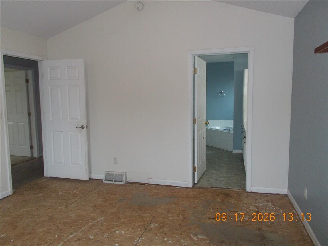 Empty room with exposed subfloor and an open doorway to a bathroom with a bathtub.