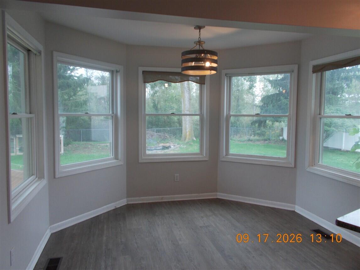 Empty dining nook with gray plank flooring, a pendant light, and five windows overlooking the backyard.